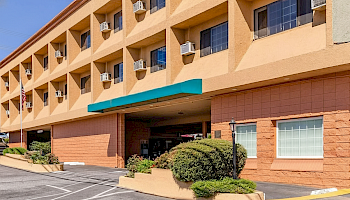 A beige multi-story motel/hotel with a teal canopy over the entrance, small shrubs, and parking in front.